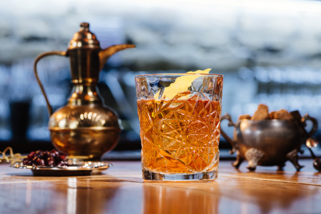 Old fashioned cocktail on a counter with a pitcher and bowl