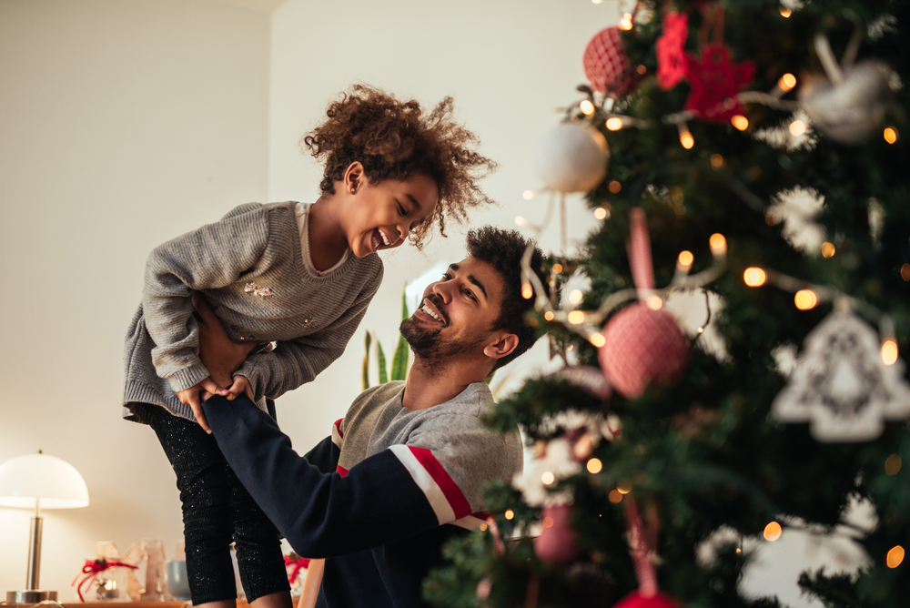 Father and daugher next to christmas tree laughing and smiling