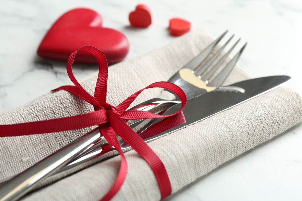 Fork and knife wrapped in red bow next to red hearts